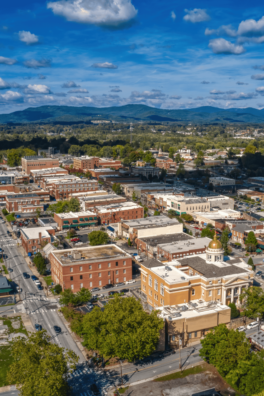 Historic downtown cityscape with mountains and blue sky in the background, featuring local businesses and architecture.