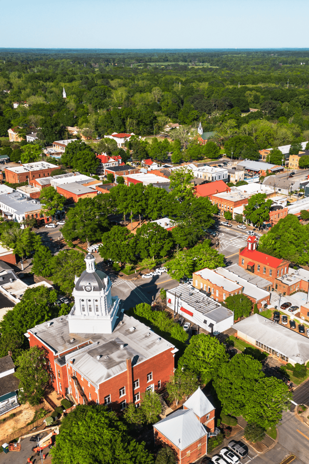 Aerial view of a small town with historic buildings, lush green trees, and downtown streets.