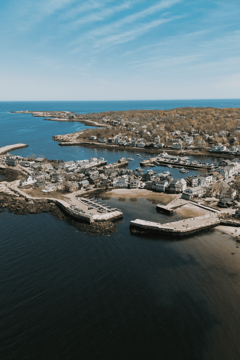 Aerial view of coastal town with marina, waterfront homes, and ocean backdrop in a scenic destination.