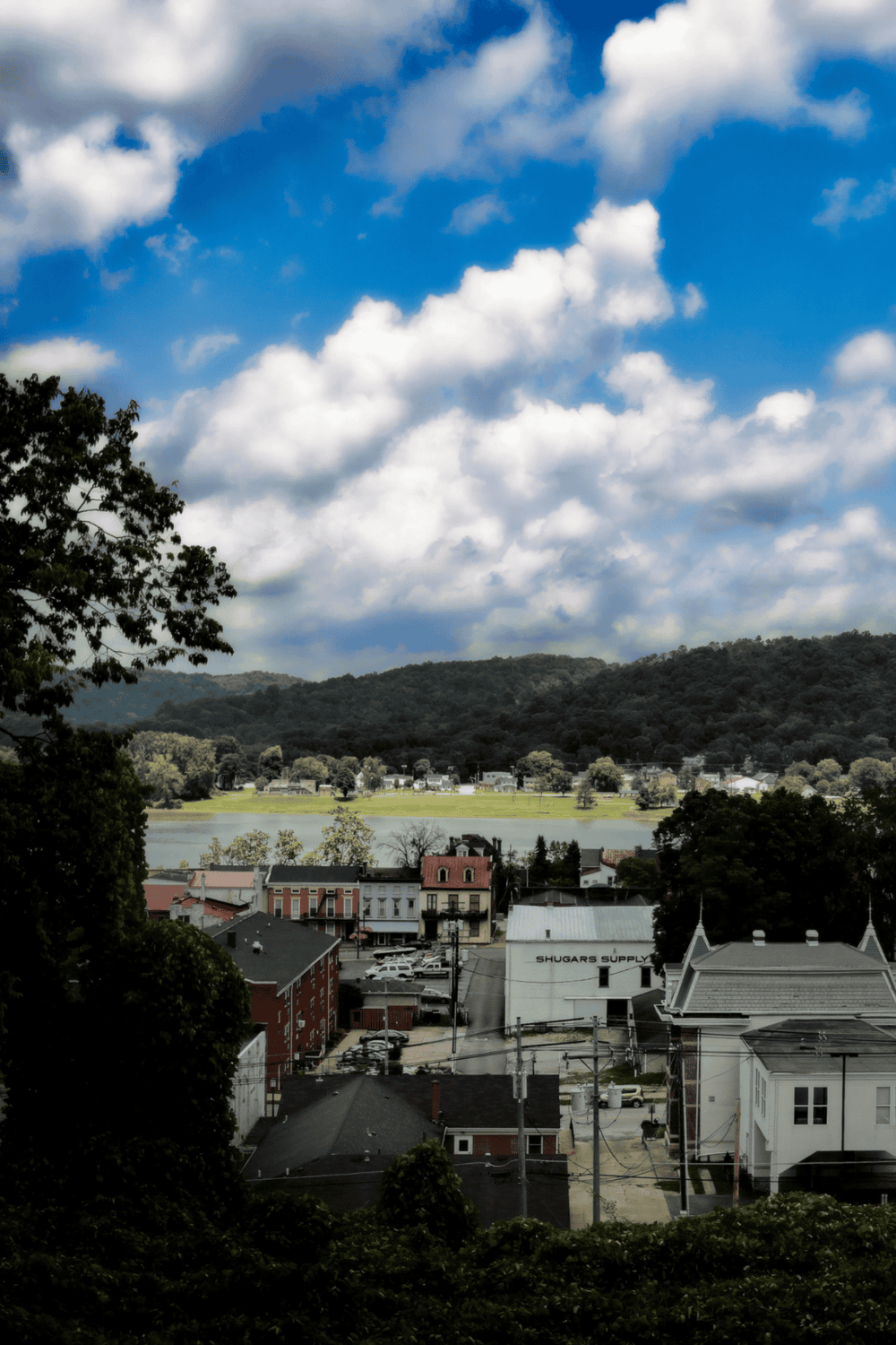 Vibrant small town with historic buildings, scenic lake, and lush green mountains under partly cloudy sky.