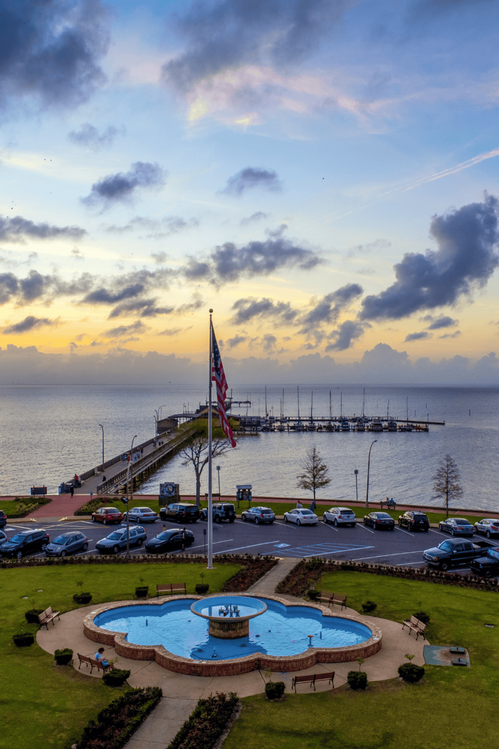 American flag at seaside pier overlooking boats and sunset sky.