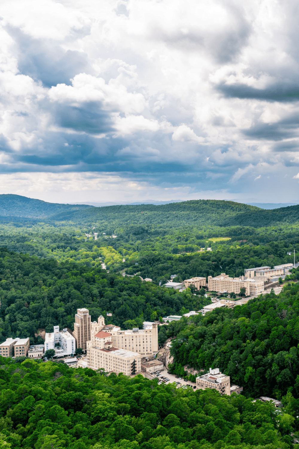 Scenic view of downtown amidst lush green hills with dramatic cloudy sky in background.