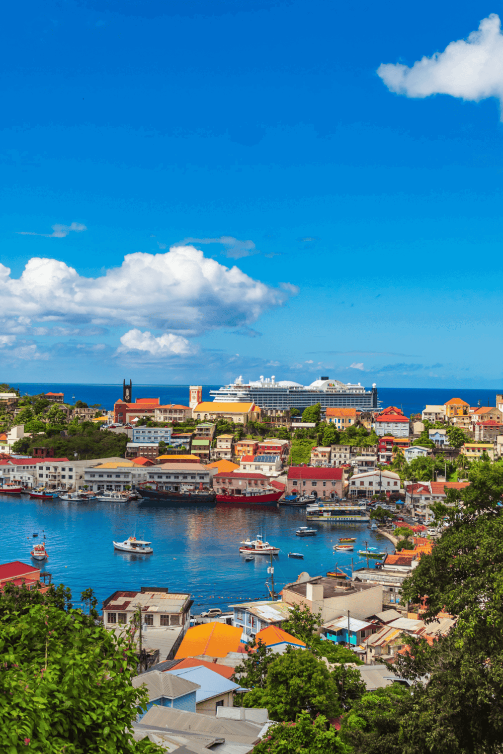 Vibrant Caribbean harbor city with colorful buildings, boats, and cruise ships under a clear blue sky.