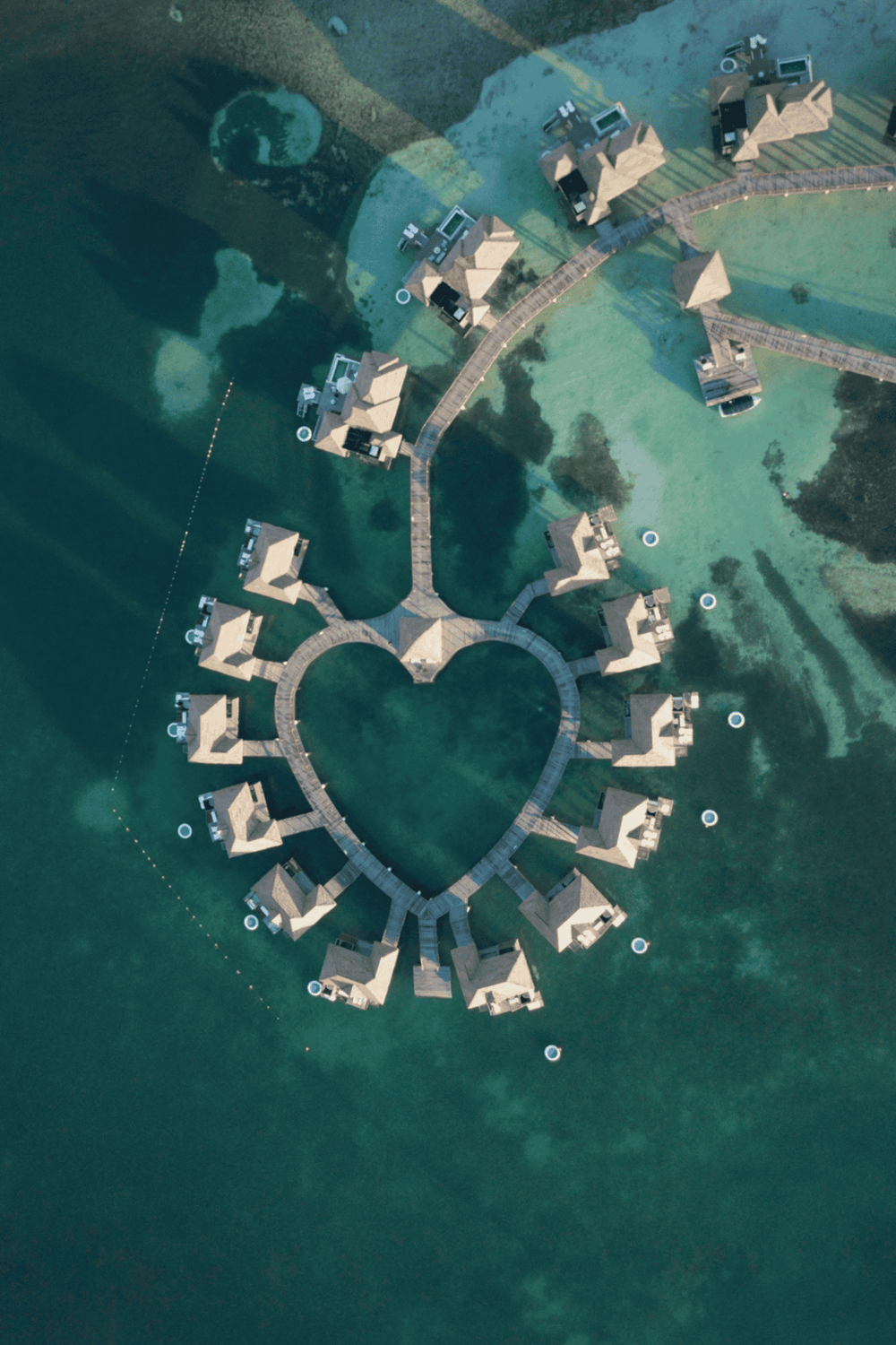 Overwater bungalows with heart-shaped pier over turquoise ocean, luxury island resort.