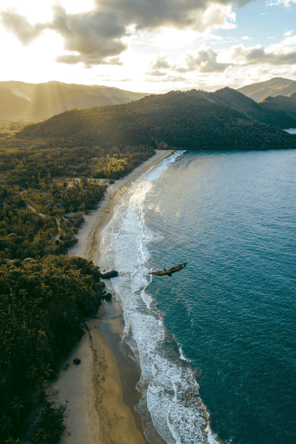 Secluded tropical beach with lush green mountains and golden sunset, perfect for travel and adventure.