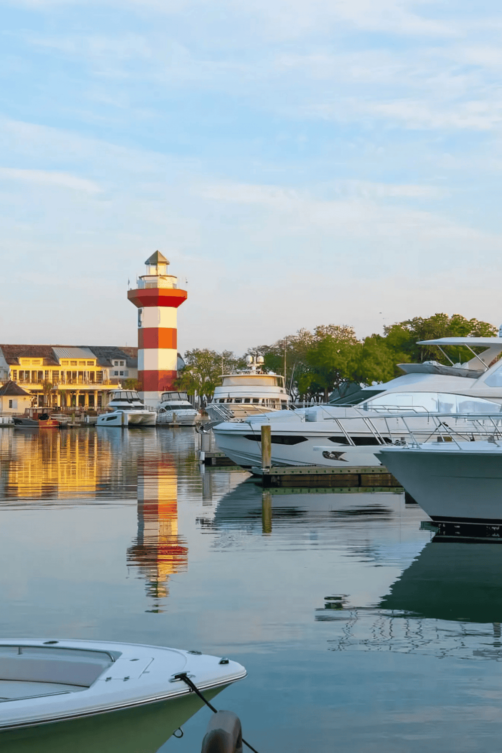 Marina with boats and a red-and-white lighthouse at sunset, scenic coastal view.