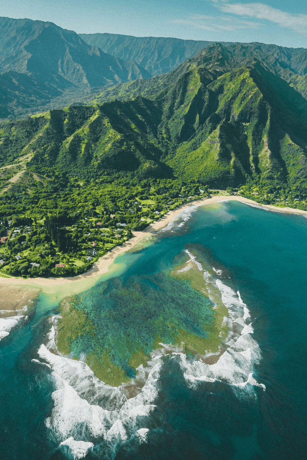 Lush green mountainous landscape with a coastline and ocean waves in Hawaii.