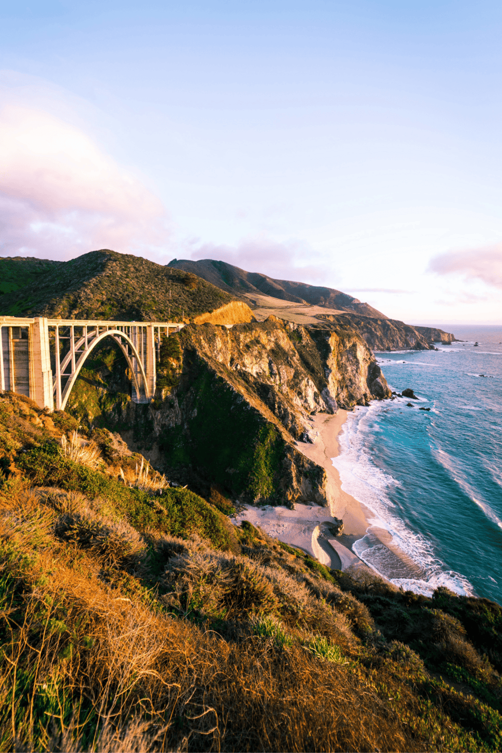 Vibrant coastal landscape with rugged cliffs, scenic beach, and the iconic Bixby Creek Bridge at sunset.