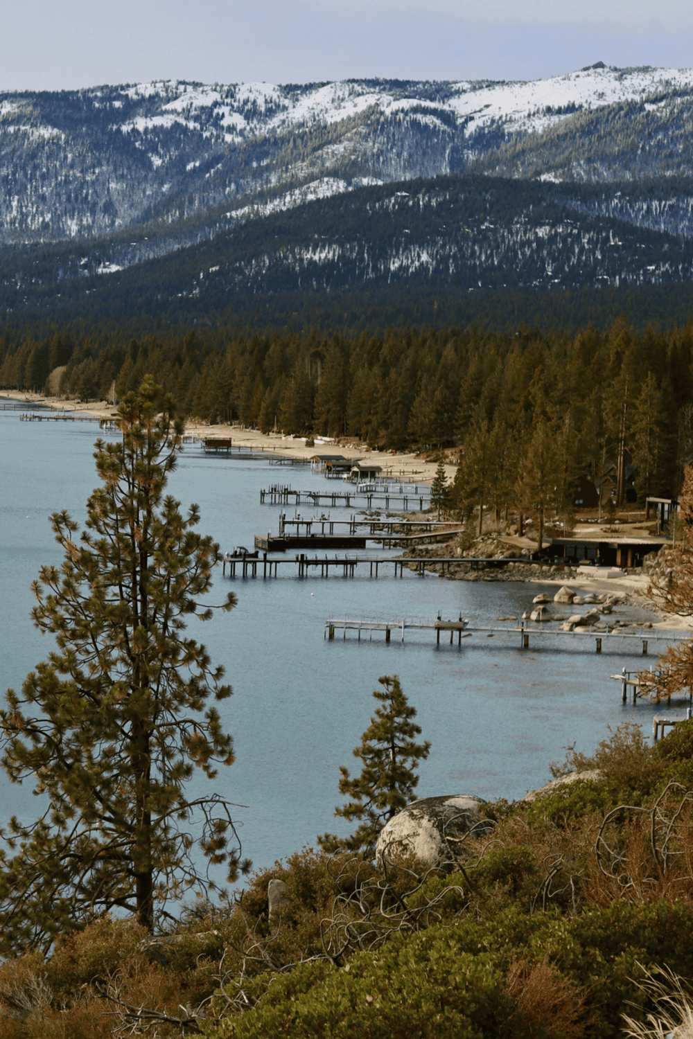 Serene lakeside view with docks, forested shoreline, and snow-capped mountains, perfect for outdoor recreation and scenic exploration.