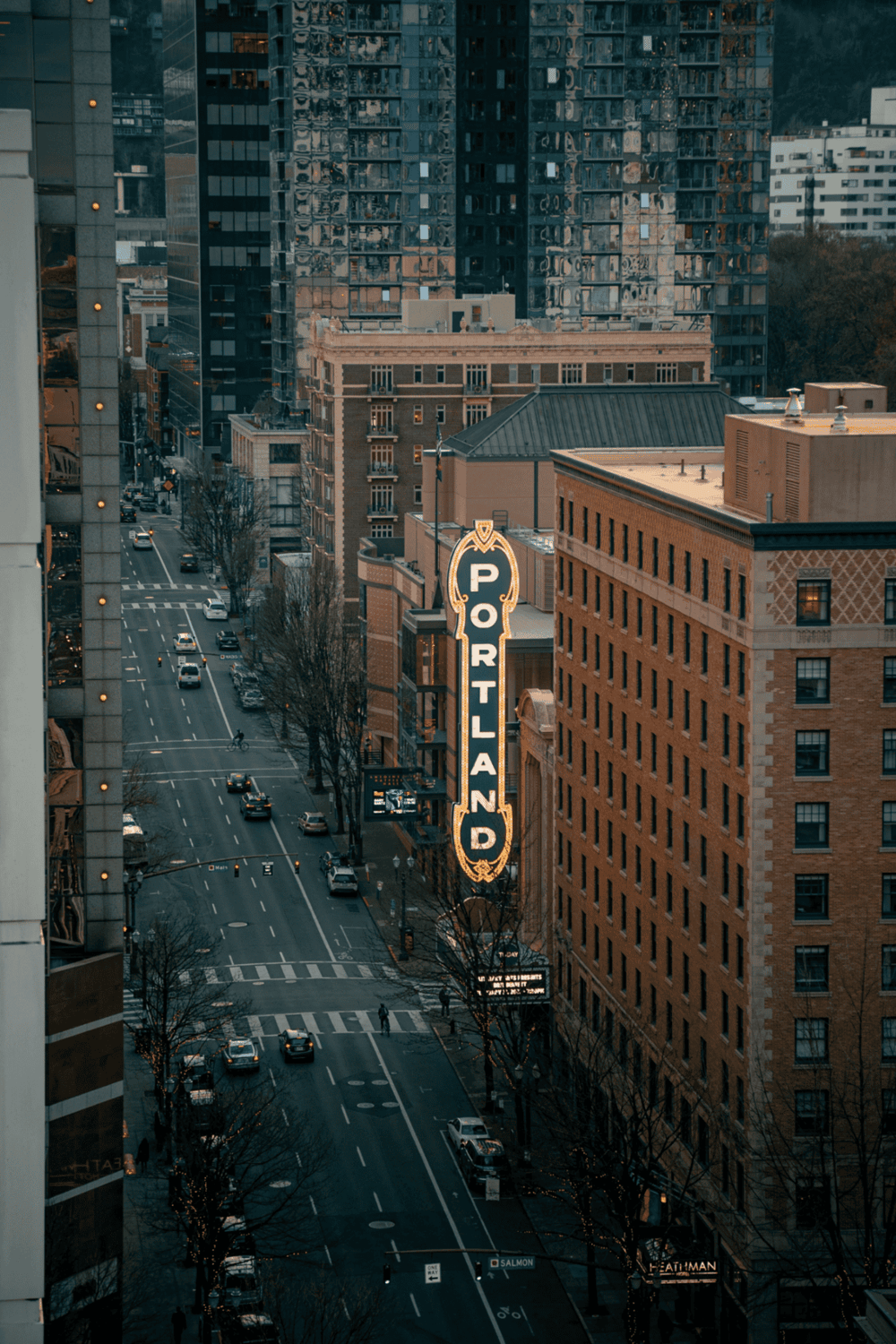 Downtown Portland skyline with historic and modern buildings, iconic Portland sign, city streets, and traffic.