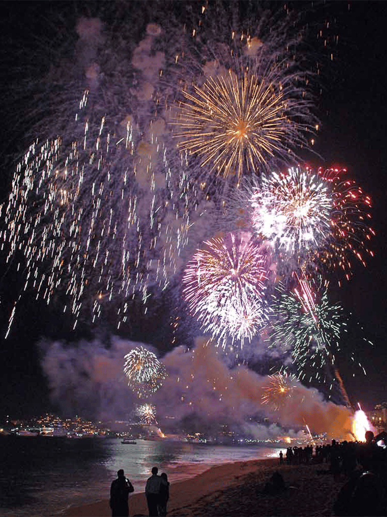 Colorful fireworks display over a beach at night, celebrating with spectators enjoying the show.