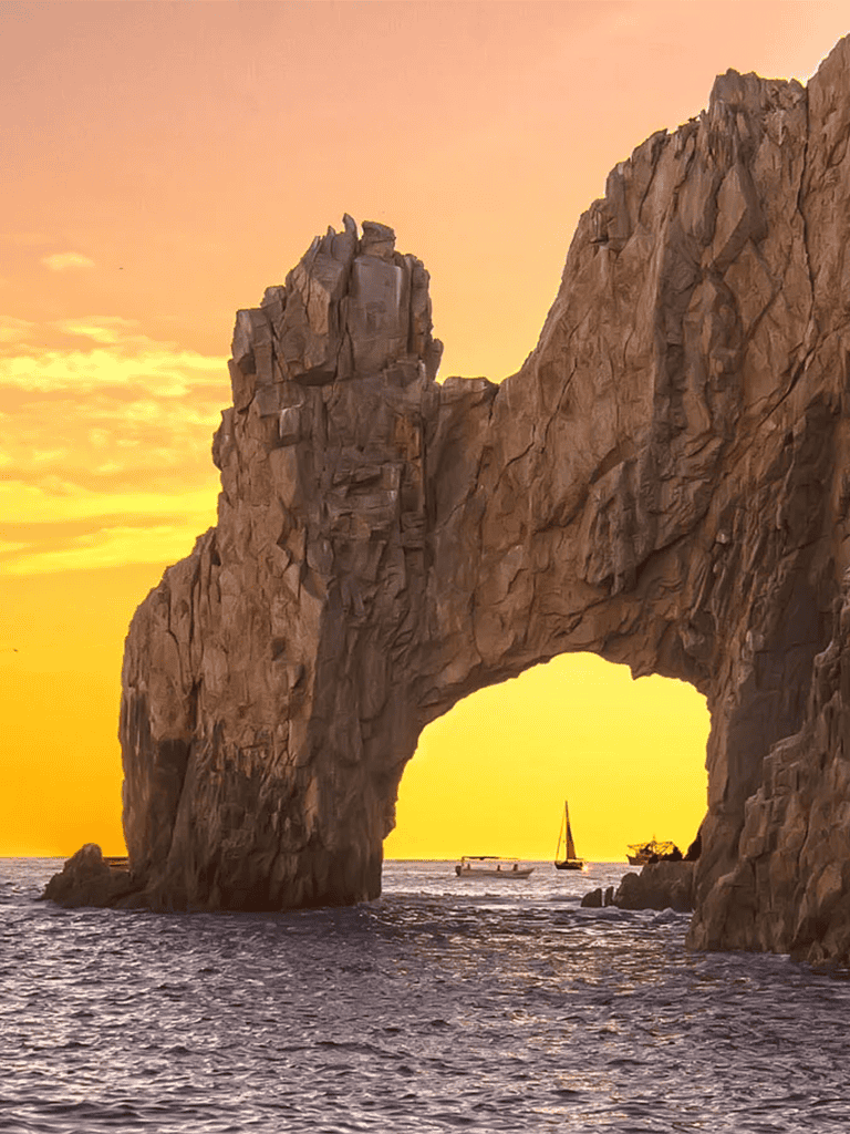 Stunning coastal rock arch at sunset, scenic ocean view with sailboat, perfect for travel and adventure photography.