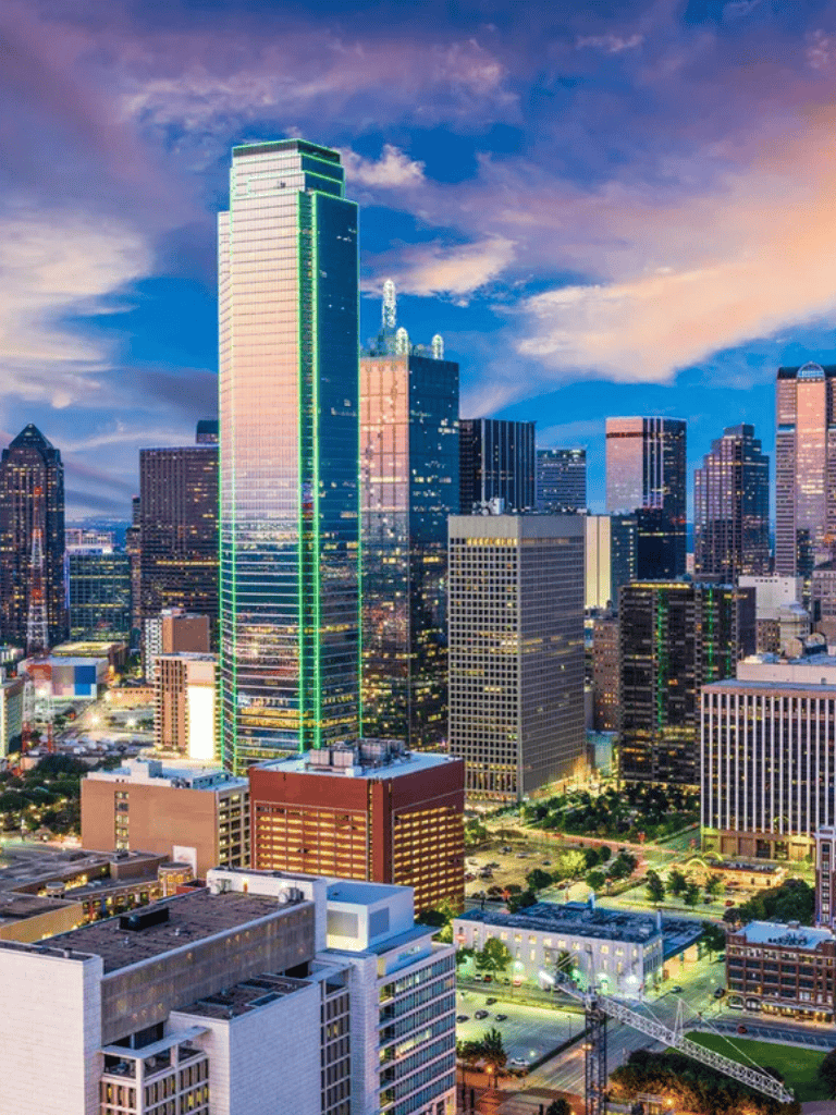 Modern downtown skyline with illuminated skyscrapers and vibrant city lights at sunset.