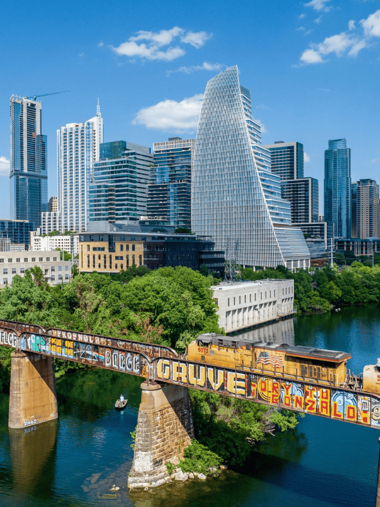Downtown Austin skyline with modern skyscrapers and colorful graffiti train on bridge over water.