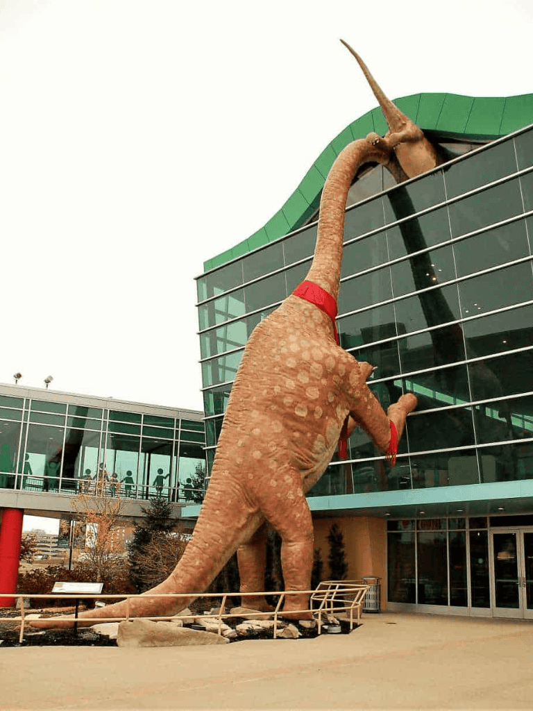 Giant dinosaur sculpture outside Quest for Directions building, modern architecture, urban outdoor scene.
