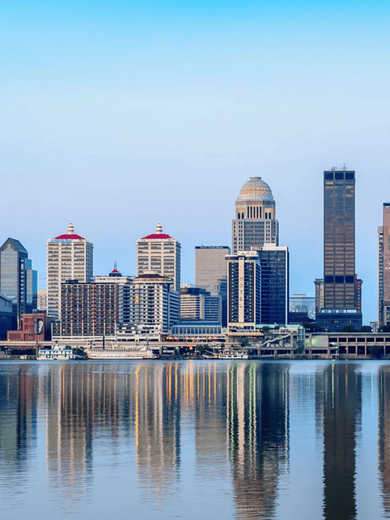 Modern city skyline with skyscrapers reflecting on water at dusk.