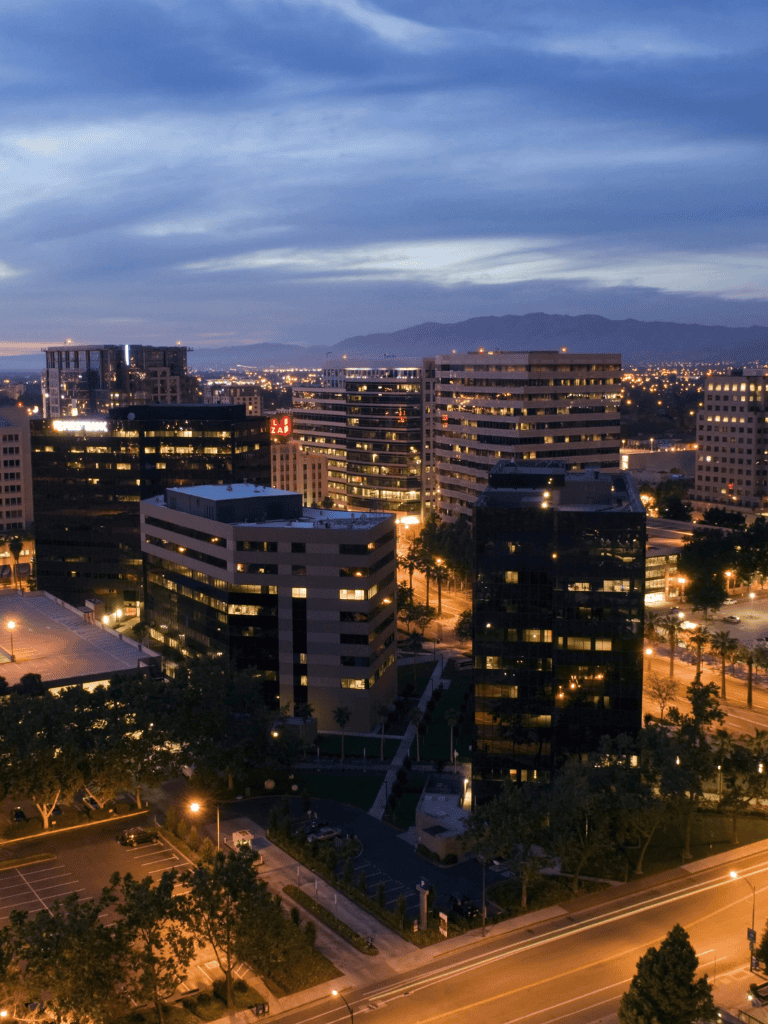 Night cityscape of modern office buildings with illuminated windows and surrounding streets, downtown urban area.