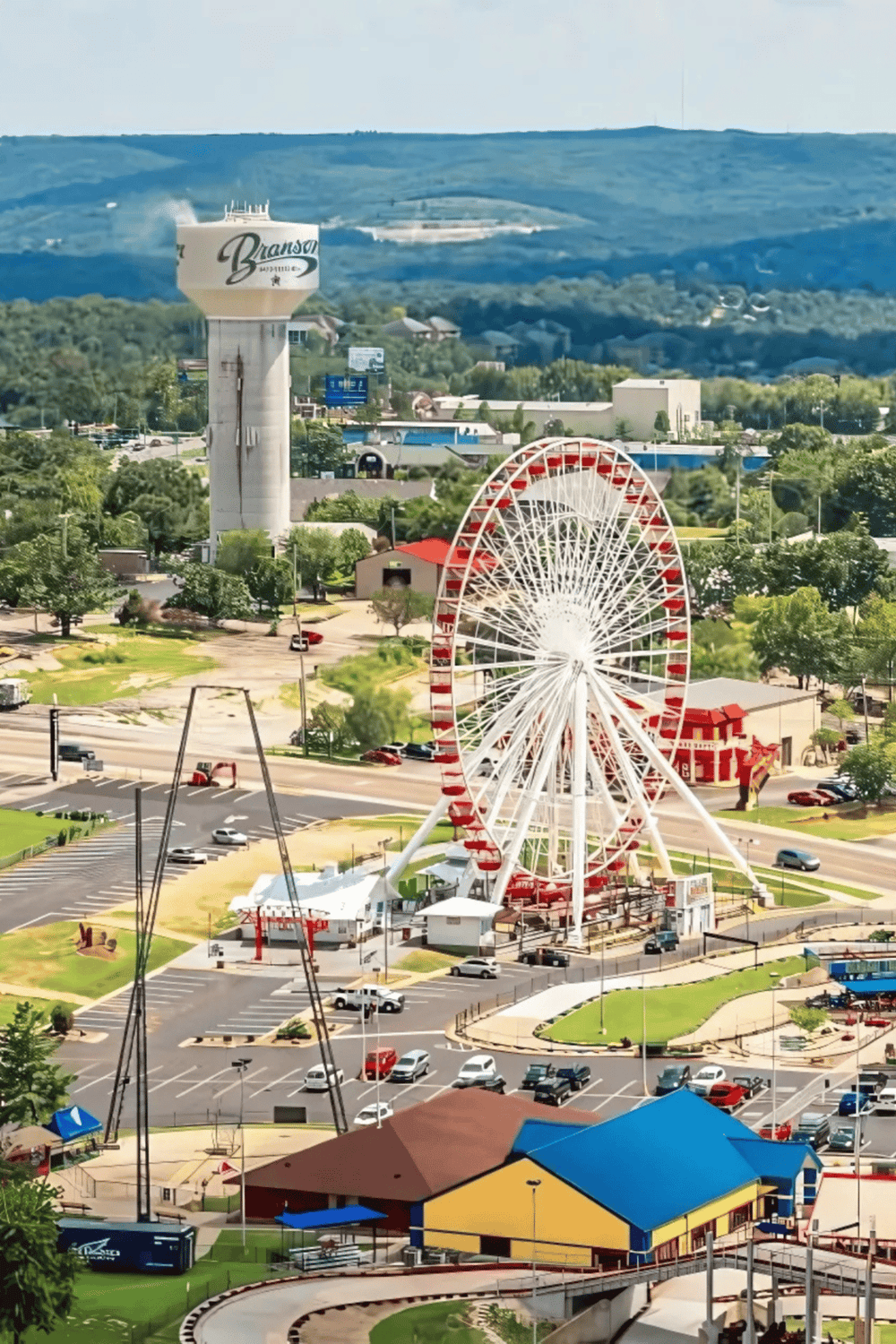 Amusement park with Ferris wheel, water tower, and attractions in a scenic town setting.