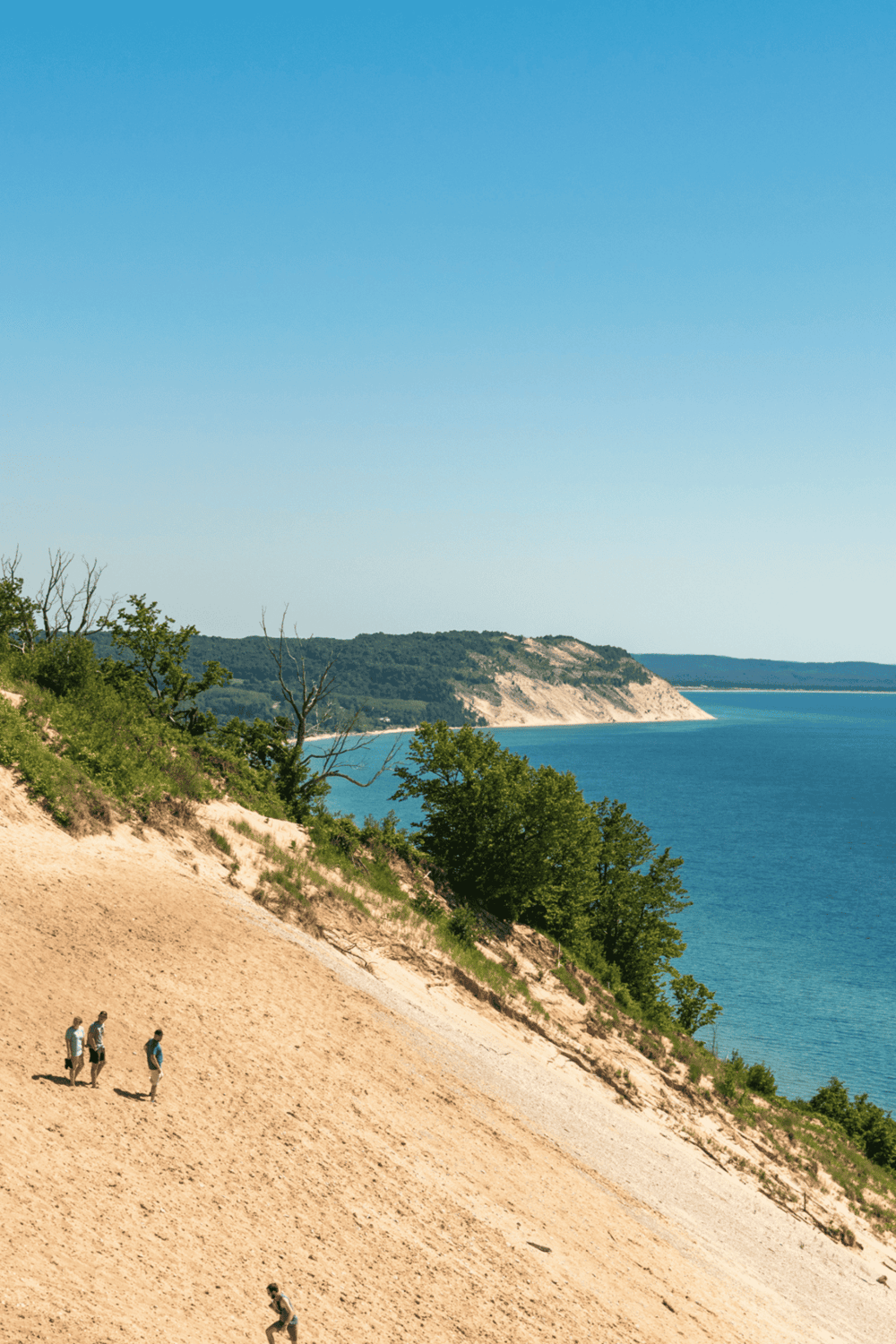 Serene lake landscape with cliffs, green trees, and hikers exploring a scenic outdoor trail.