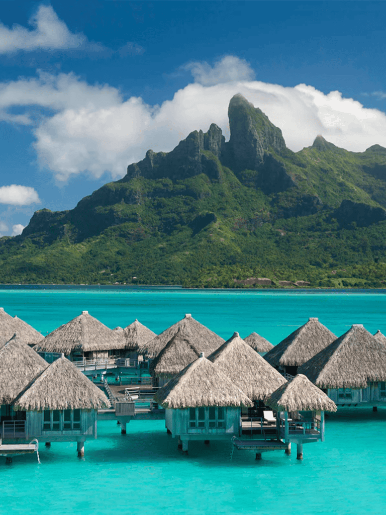 Overwater bungalows overlooking a tropical island mountain and clear turquoise waters.