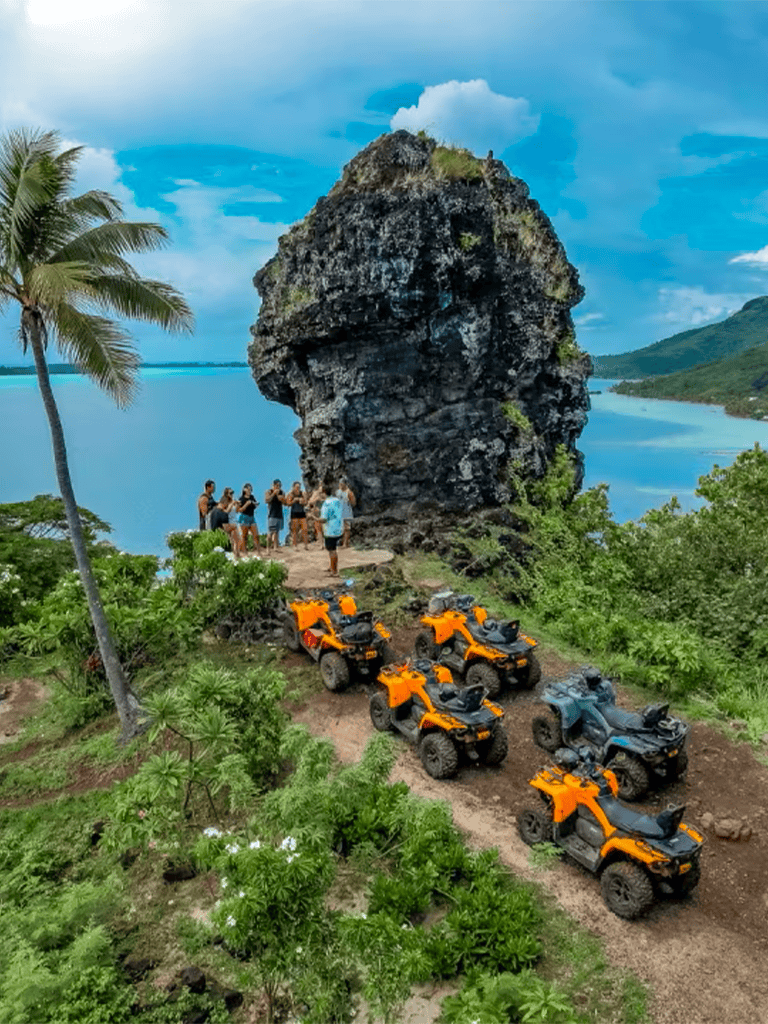 Vibrant outdoor adventure scene with atvs, lush greenery, ocean view, and a group of tourists taking photos.