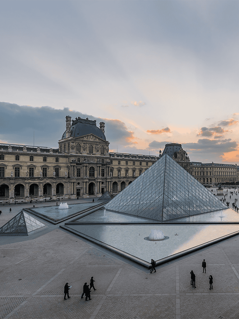 Majestic Louvre Museum with glass pyramids in Paris at sunset, popular tourist destination.