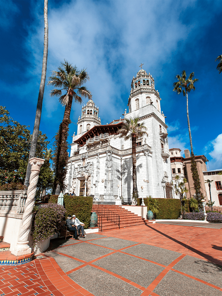 Magnificent white historic church with tall towers, surrounded by palm trees and vibrant blue sky.