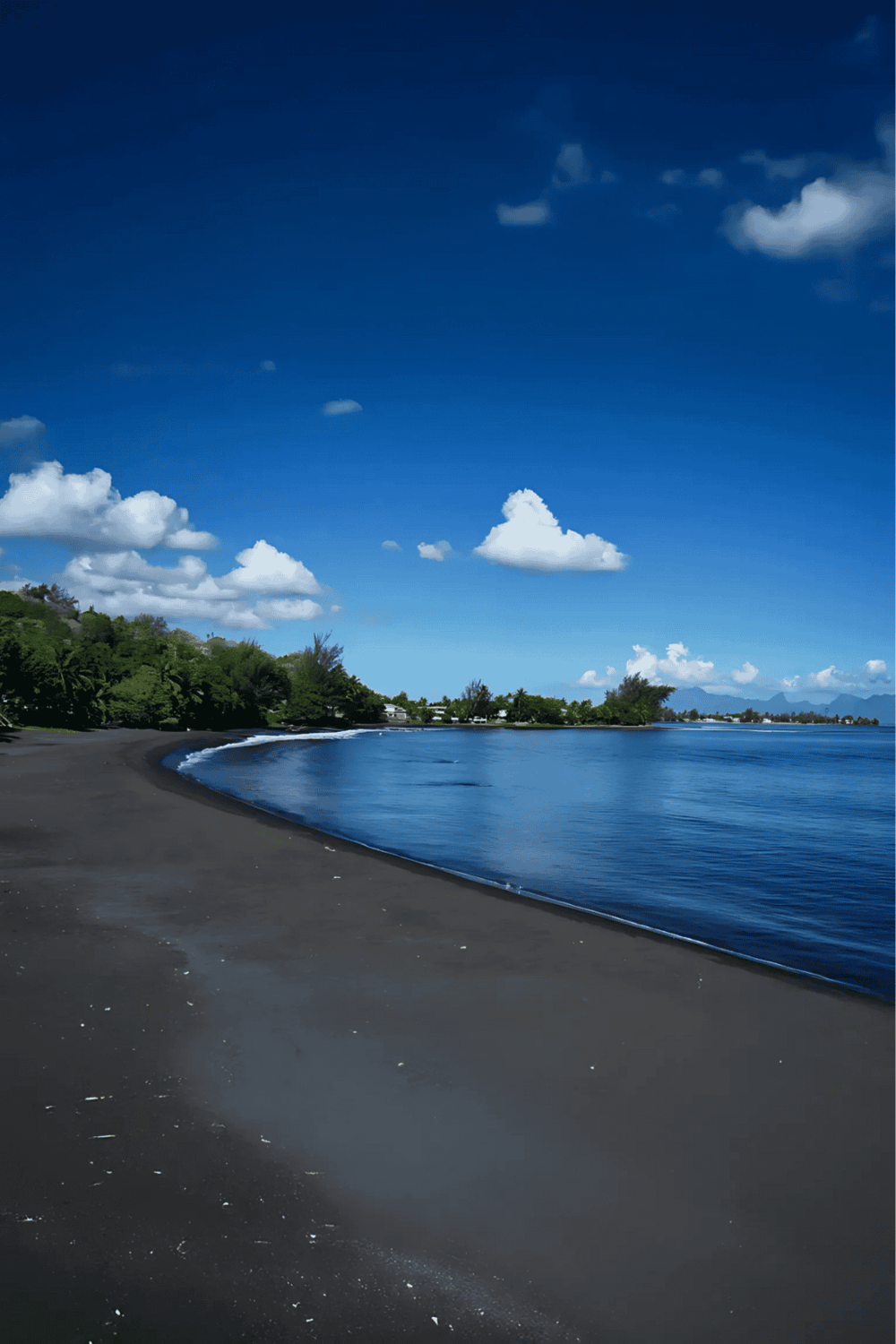 Serene beach with dark sand, lush greenery, and clear blue sky, perfect for travel and outdoor adventures.