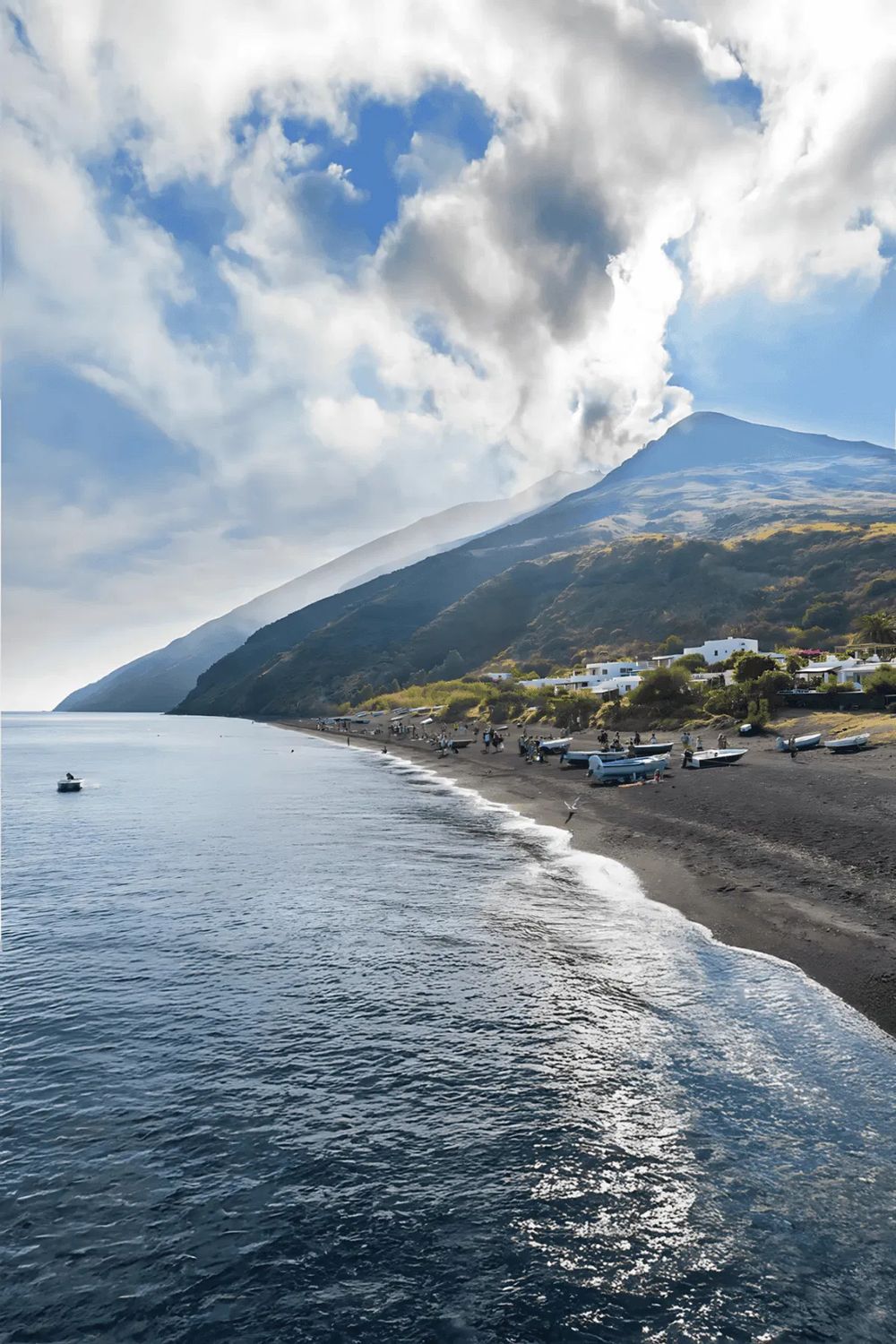 Majestic coastal mountain view with boats on the black sand beach, perfect for travel inspiration and adventure seekers.