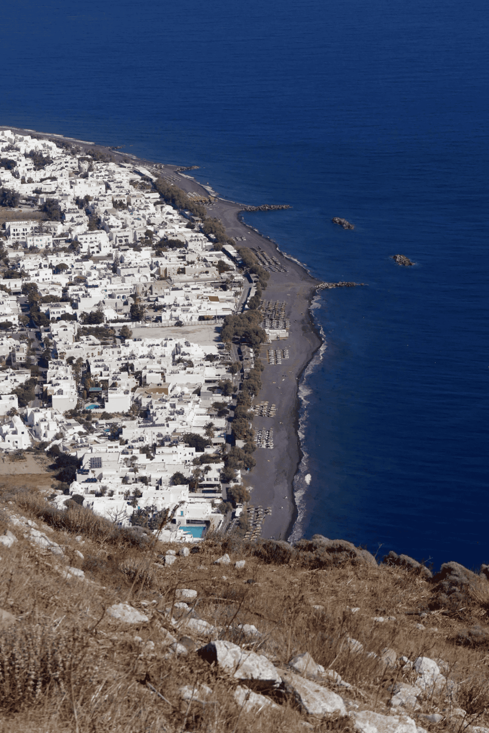Aerial view of Santorini's coastline with white buildings and deep blue Aegean Sea.