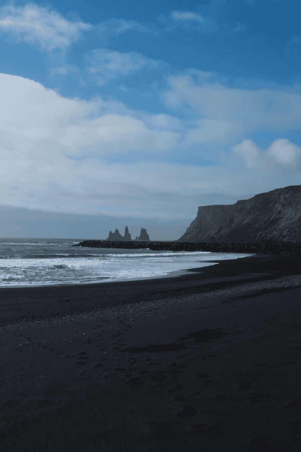 Dark volcanic beach with ocean waves and volcanic cliffs, Iceland.