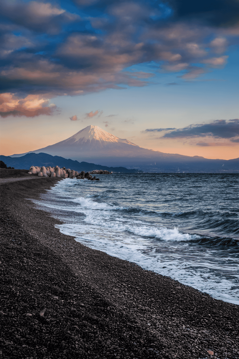 Snow-capped Mount Fuji view from rocky shoreline, Japan travel destination, scenic mountain and ocean vista, outdoor adventure.