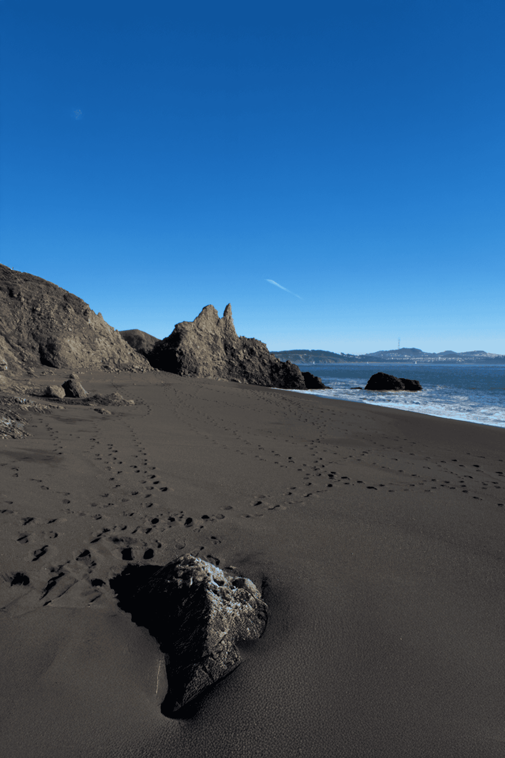 Secluded beach with large rock formations, footprints in sand, and clear blue sky, perfect for coastal exploration and relaxation.