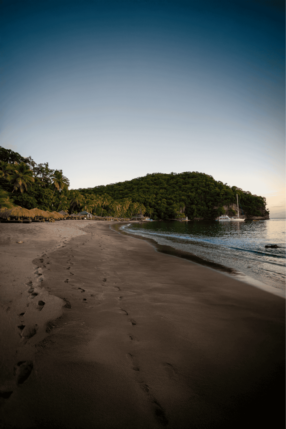 Serene beach with footprints, lush green island, and calm ocean in the sunset light.