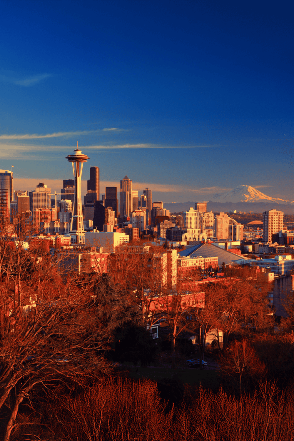 Seattle skyline with Space Needle and Mount Rainier in background, vibrant sunset lighting.