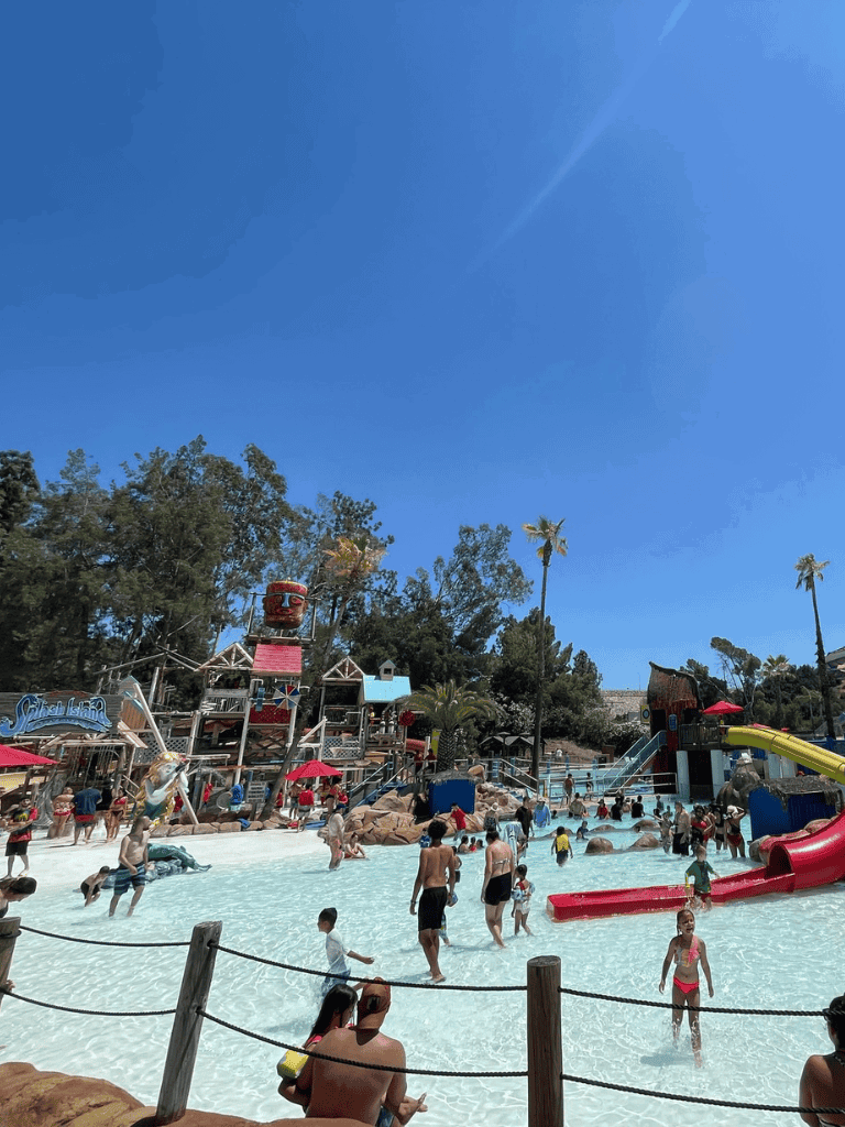 Open-air water park with slides and desert landscaping, sunny sky, families enjoying water activities.