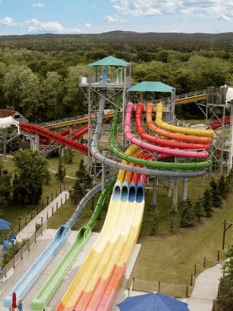 Colorful water slides at an amusement park with lush green surroundings and hills in the background.
