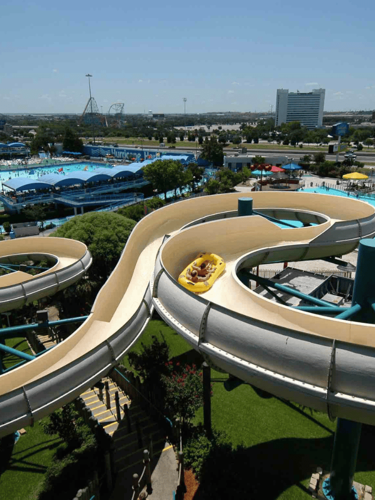 Water park water slide with a yellow raft, open park scenery in the background, bright sunny day.