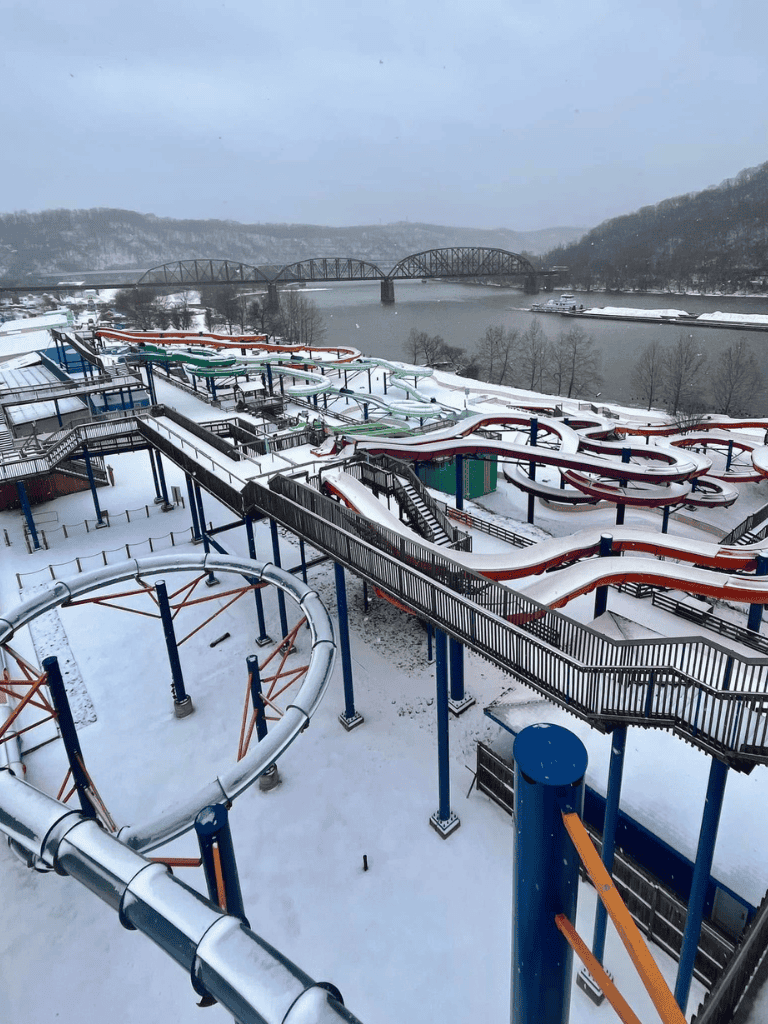Snow-covered water park with water slides and bridge over river, winter scene.