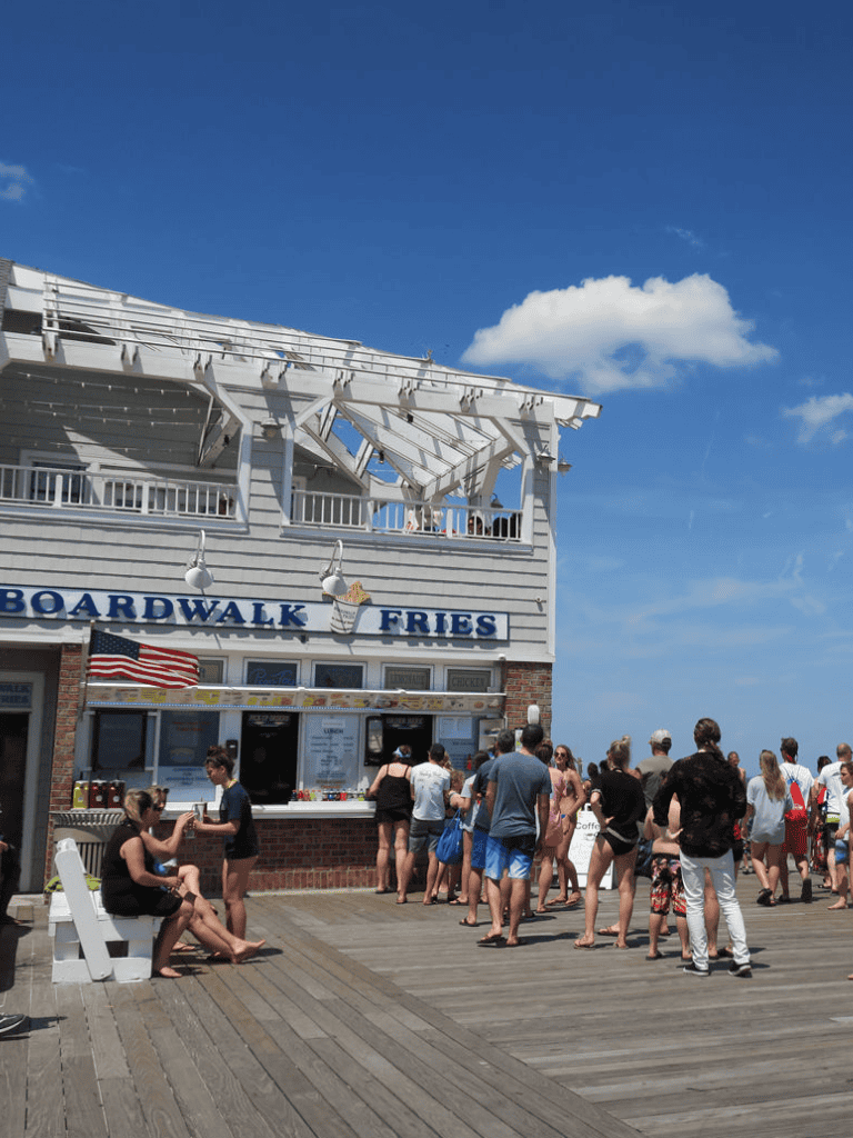 Outdoor boardwalk food stand at the seaside with people enjoying a sunny day.