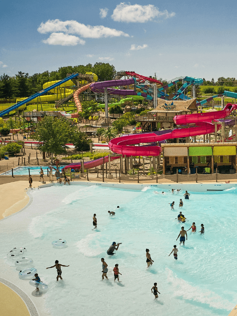 Colorful water slides at a lively water park with children swimming and playing in the wave pool.