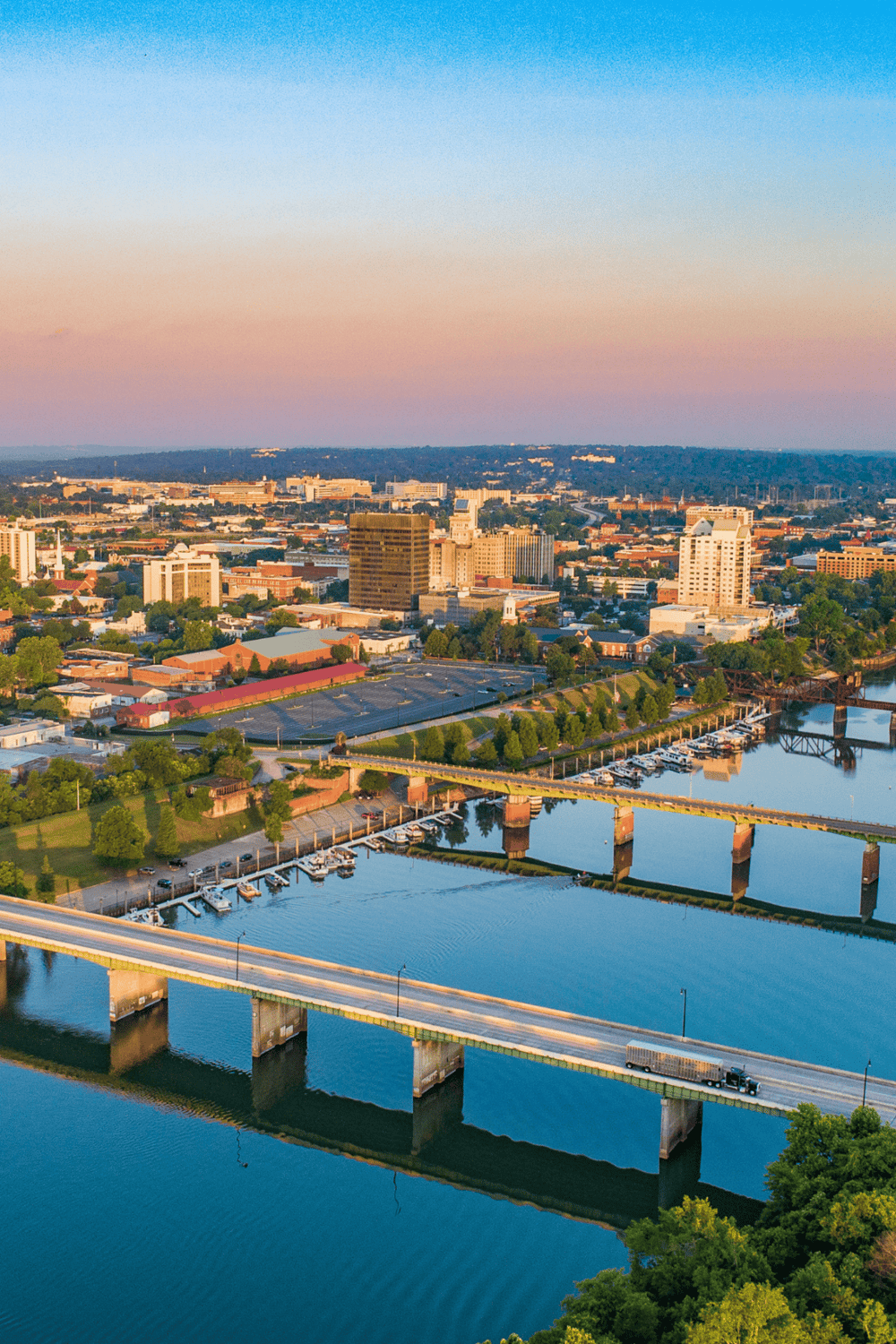Aerial view of a city skyline with river, bridges, and downtown buildings at sunset.