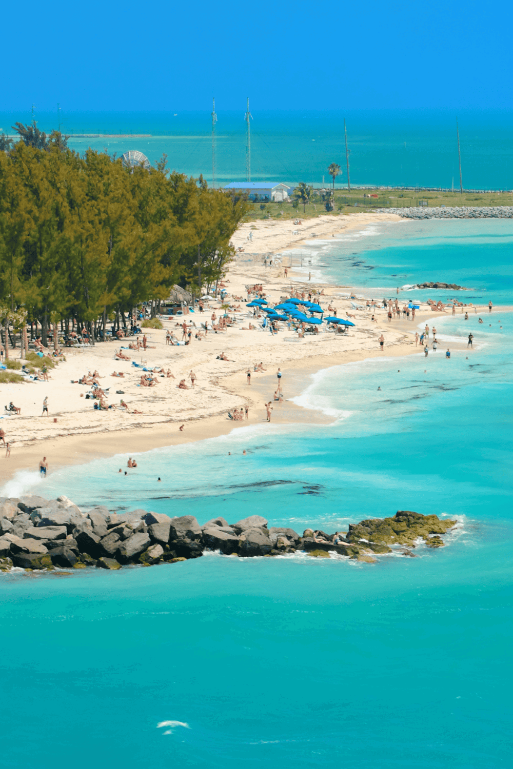 1. Beach scene with turquoise waters, blue umbrellas, and people enjoying the sunny day.