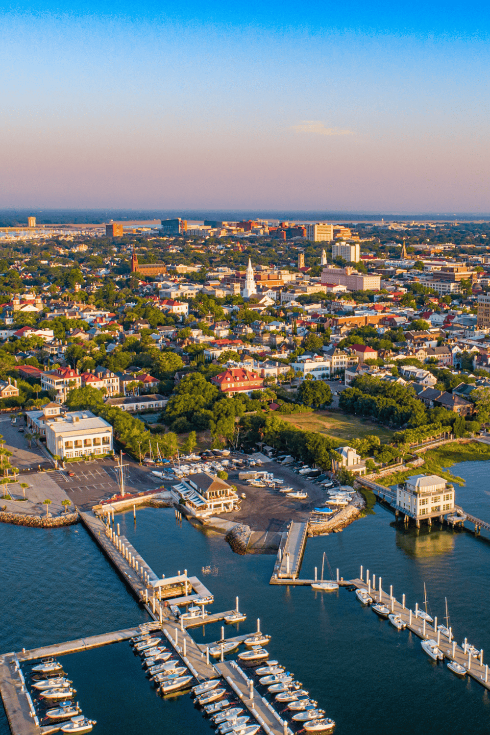 Aerial view of a waterfront cityscape with marina, boats, and lush green neighborhoods, showcasing scenic urban and coastal attractions.