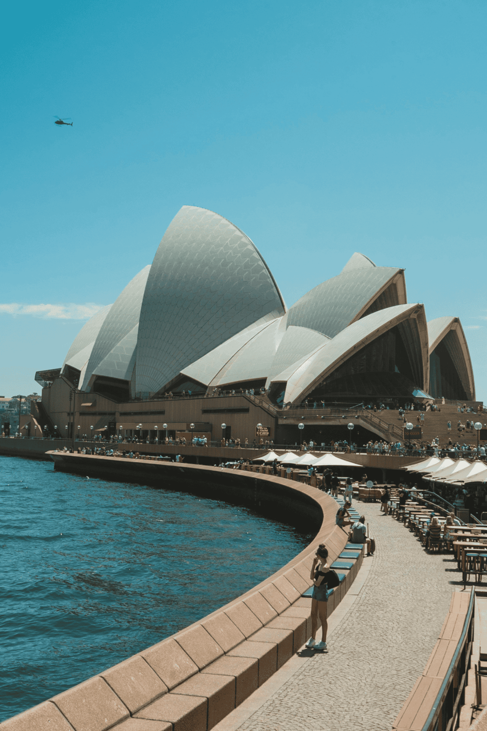 Iconic Sydney Opera House with waterfront views and tourist visitors.