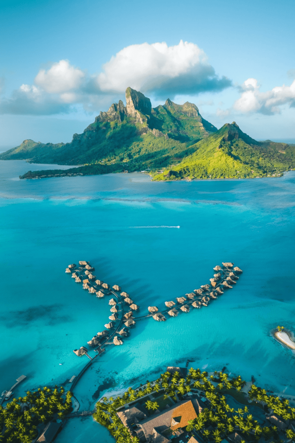 Overwater bungalows at a tropical island resort with lush mountains and turquoise ocean.