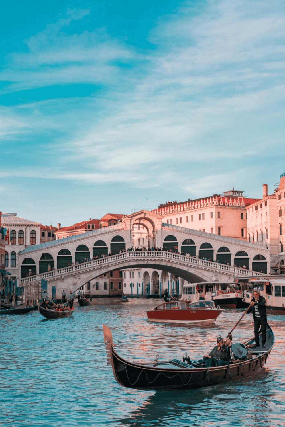 Gondolas floating under the Rialto Bridge in Venice, Italy, during sunset, showcasing iconic Venetian scenery.