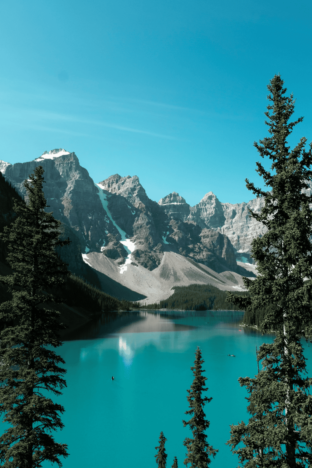 Serene mountain lake with forested shoreline and snow-capped peaks, scenic outdoor adventure destination.