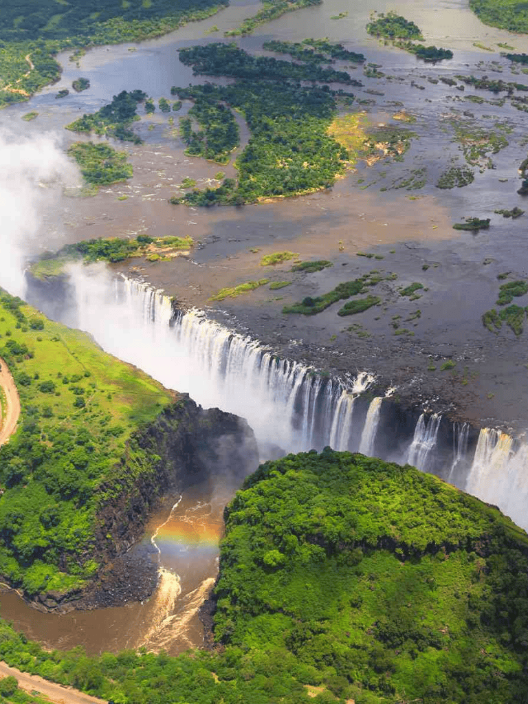 Aerial view of Victoria Falls on the Zambezi River, lush greenery surrounding the iconic waterfall.