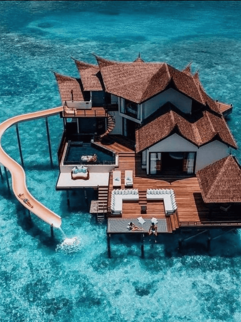 Luxurious overwater villa with pool and waterslide in tropical ocean setting.